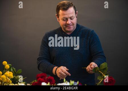 Fiorista caucasico che vende bouquet di rose rosse e rosa per la giornata di San Valentino. Concetto di emozioni umane, espressione facciale, amore e duro lavoro Foto Stock