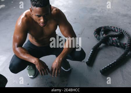 L'uomo afroamericano indossa abiti sportivi che squattano riposandosi dopo la battaglia funi in buu. urbano vuoto Foto Stock