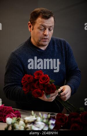 Fiorista caucasico che vende bouquet di rose rosse e rosa per la giornata di San Valentino. Concetto di emozioni umane, espressione facciale, amore e duro lavoro Foto Stock