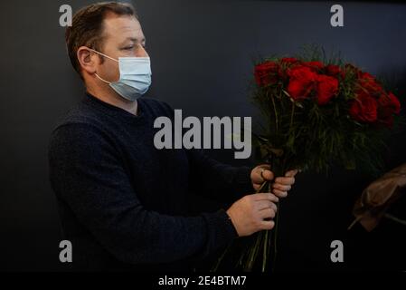 Fiorista caucasico che vende bouquet di rose rosse e rosa per la giornata di San Valentino. Concetto di emozioni umane, espressione facciale, amore e duro lavoro Foto Stock