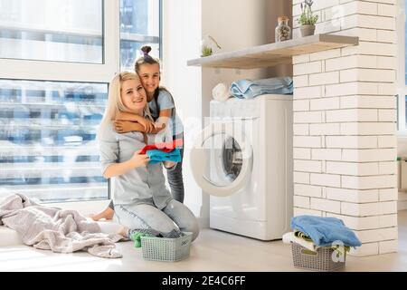 Happy housewife and her daughter with linen near washing machine Stock Photo