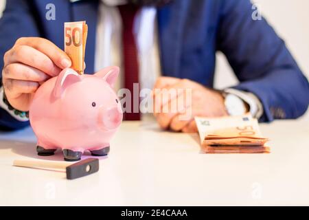 Uomo d'affari che mette cinquanta euro banconote in banca piggy. Concetto finanziario e risparmio di denaro Foto Stock