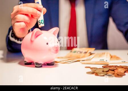 Uomo d'affari che mette cinquanta euro banconote in banca piggy. Concetto finanziario e risparmio di denaro Foto Stock