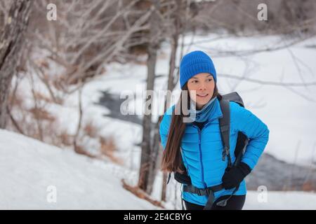 Inverno escursioni donna asiatica escursionista camminare sulla neve sentiero escursionistico nella foresta all'aperto. Zaino con giacca blu e zaino con cappello Foto Stock