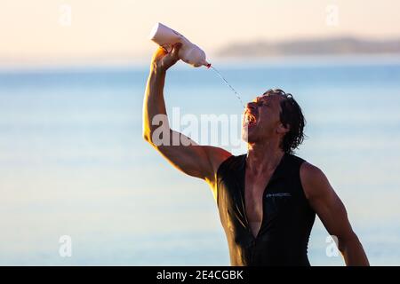 Man 50 Plus FIT, con una muta in mare, beve dalla sua bottiglia d'acqua. Foto Stock