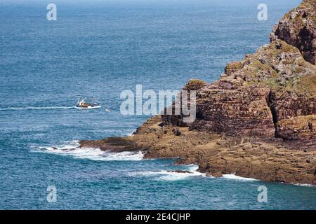 Una barca da pesca va intorno alle scogliere di Cap Frehel. Bretagna, Francia Foto Stock