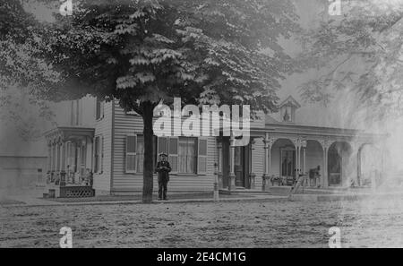 Archivio americano foto monocromatica di un uomo che si trova fuori di una grande casa di ciottoli con portici. Preso nel tardo 19 ° secolo a Port Byron, New York, Stati Uniti Foto Stock