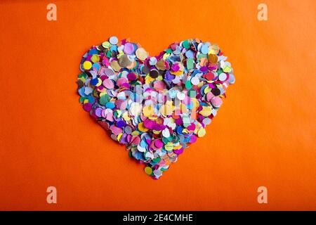 concetto d'amore immagine della forma del cuore fatta di confetti colorati su sfondo arancione di trama della carta Foto Stock