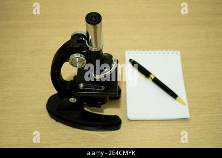 Microscopio nero sulla scrivania con un notebook e un penna accanto ad essa Foto Stock