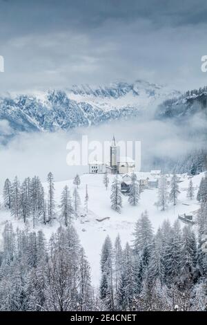 Italia, Veneto, provincia di Belluno, Rocca Pietore, Agordino, il paese di Laste in inverno con la chiesa di San Gottardo sulla collina, Dolomiti Foto Stock