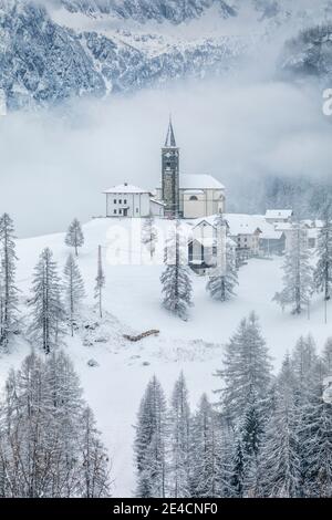 Italia, Veneto, provincia di Belluno, Rocca Pietore, Agordino, il paese di Laste in inverno con la chiesa di San Gottardo sulla collina, Dolomiti Foto Stock