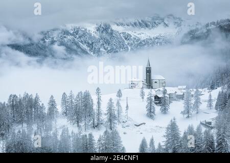 Italia, Veneto, provincia di Belluno, Rocca Pietore, Agordino, il paese di Laste in inverno con la chiesa di San Gottardo sulla collina, Dolomiti Foto Stock