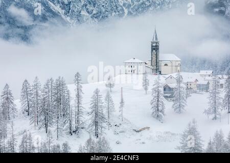 Italia, Veneto, provincia di Belluno, Rocca Pietore, Agordino, il paese di Laste in inverno con la chiesa di San Gottardo sulla collina, Dolomiti Foto Stock