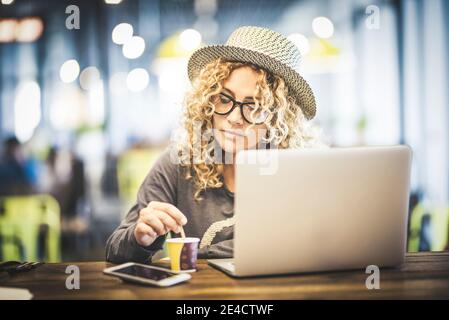 Bella giovane donna adulta al lavoro con computer portatile coimputer dentro un cafe ristorante all'aeroporto che aspetta il suo volo viaggiare - nomade digitale e lavoro online persone moderne concetto di tecnologia Foto Stock
