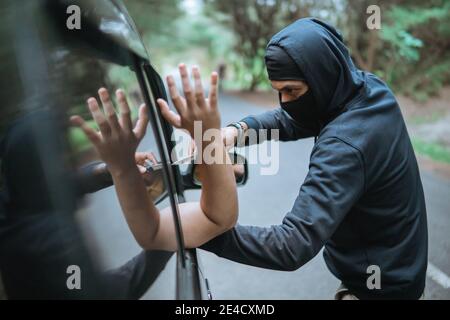 ladro criminale in strada tenendo coltello vicino auto su tranquillo via Foto Stock