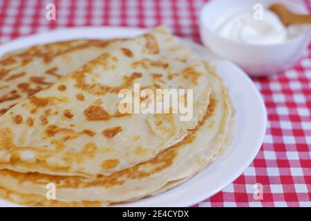 Deliziosi pancake di cucina russa su un piatto e dolce sour panna in una tazza con un cucchiaio di still-life Foto Stock