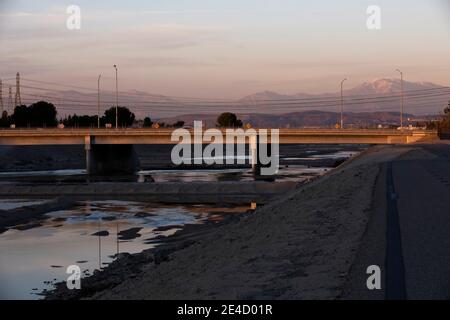 Vista al tramonto del fiume Santa Ana mentre si snoda attraverso Anaheim con montagne innevate in lontananza. Foto Stock