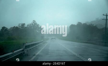 Una scena sfocata di pioggia che cade sul parabrezza di un'auto mentre viaggia lungo una strada suburbana - intenzionalmente sfocata per effetto. Foto Stock