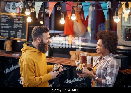 gli amici parlano e ridono mentre mangiano i panini davanti al servizio fast food. all'aperto Foto Stock