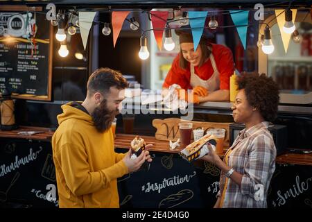 felice dipendente in fast food servizio sorridente, cercando multietchnic soddisfatti clienti dopo aver assaggiato panini Foto Stock