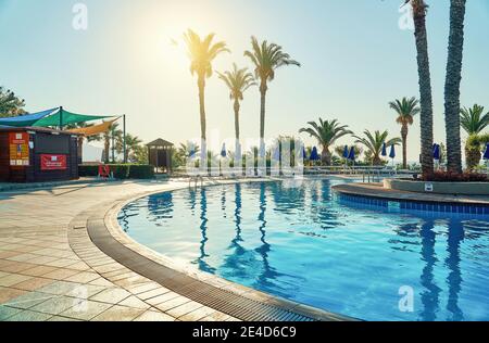 Piscina blu pulita e piscina piastrellata vicino all'hotel palme in mattinata soleggiata sulla località tropicale in estate Foto Stock