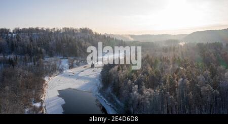 Ripresa panoramica di una strada curvilinea su un fiume che scorre attraverso la foresta innevata Foto Stock