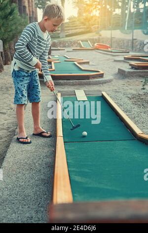 Ragazzo felice in abiti casual sorridente e guardando via mentre giocare a mini golf il giorno d'estate sul territorio di l'hotel Foto Stock