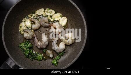 Gamberi neri di tigre o gamberetti in una padella con olio, aglio e prezzemolo sulla stufa nera, cucinando un delizioso spuntino mediterraneo, spazio copia, hi Foto Stock