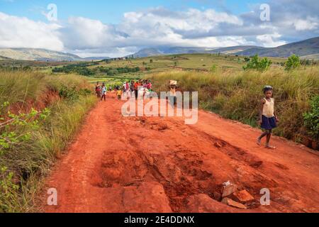 Sendrisoa, Madagascar - 28 aprile 2019: Gruppo di uomini, donne e bambini malgasci sconosciuti che camminano a casa dopo aver lavorato nei campi, sulla strada della polvere rossa, gr Foto Stock