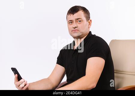 Ritratto di un uomo difficile da udire seduto in una poltrona in pelle da ufficio con uno smartphone. Sfondo bianco con spazio vuoto. Foto Stock