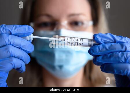 Test COVID-19 in primo piano con le mani del medico, la donna in maschera medica contiene il kit di raccolta del tampone di coronavirus in laboratorio. Concetto di diagnostica del virus corona Foto Stock