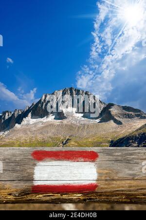 Cartello rosso e bianco dipinto su un vecchio palo di legno. Sullo sfondo la vetta del Care Alto nel parco nazionale dell'Adamello Brenta Foto Stock
