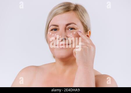 Donna bionda senior con maschera crema sotto gli occhi. Bella donna con perfetta pelle e crema contorno anti-invecchiamento e rughe occhi. Concetto di bellezza Foto Stock