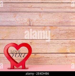 cuore rosso con un titolo al centro che mette vi innamorerete di uno sfondo in legno e di una base rosa Foto Stock
