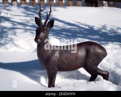 Scultura orizzontale di capriolo di bronzo in piedi nella neve. Foto Stock
