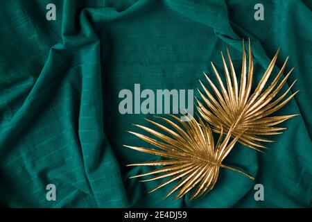 Concetto creativo di due rami con foglie di palma d'oro su uno sfondo ciano scuro. Foto Stock