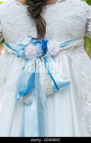 Pizzo testurizzato sul retro di un abito bianco ragazza con arco con fiori blu. Foto Stock