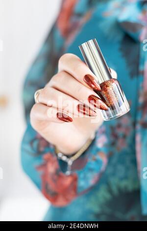 Mano femminile con unghie lunghe e marrone dorato, manicure contiene una bottiglia di smalto per unghie Foto Stock