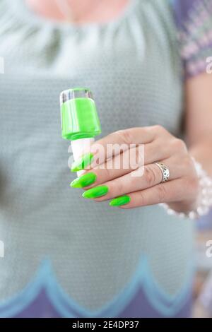 Mano femminile con unghie lunghe e manicure verde al neon con bottiglie di smalto per unghie Foto Stock