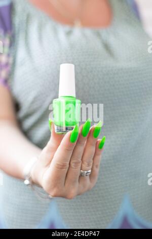 Mano femminile con unghie lunghe e manicure verde al neon con bottiglie di smalto per unghie Foto Stock