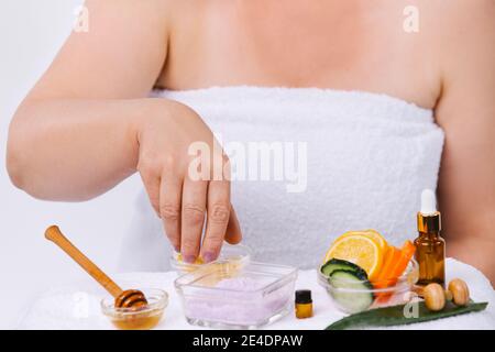 Foto ingrandita delle mani femminili senior che fanno un scrub a casa da prodotti naturali. Sfondo bianco. Concetto domestico di cura della pelle. Foto Stock