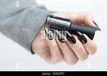 Mano femminile con unghie lunghe e maniglie in manicure grigio nero una bottiglia di smalto per unghie Foto Stock