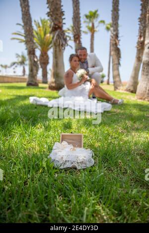 Anelli di nozze isolati posati sul prato con la sposa e lo sposo dietro Foto Stock