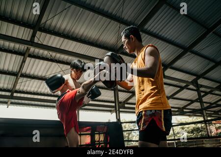 kickboxer e allenatore insieme con i pattini di punzonatura alla boxe campo di allenamento Foto Stock