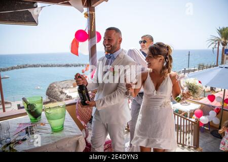 Una coppia appena sposata apre la bottiglia di champagne per celebrare il loro matrimonio. Foto Stock