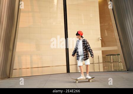 teenage asiatico ragazzo di quindici anni skateboarding di fronte a un edificio moderno Foto Stock