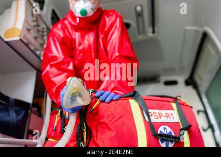 Paramedico maschile con maschera facciale che aiuta un paziente con respiratore in ambulanza durante la pandemia. Un ritratto di paramedico seduto in un'auto ambulanza. Foto Stock