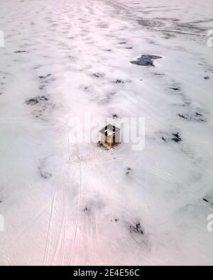 Vista aerea di una piccola capanna di legno al centro di un campo ghiacciato innevato con piste da sci Foto Stock