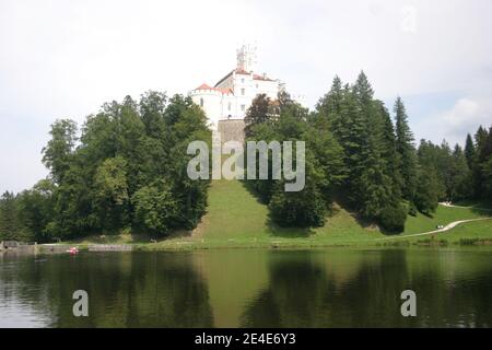 Un castello medievale sul lago, in cima alla collina, circondato da boschi; foto scattata in una giornata nuvolosa d'estate Foto Stock