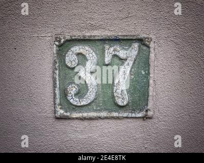 Numero 37, il numero di case, appartamenti, strade. Il numero bianco su una piastra di metallo verde, il numero civico trentasette (37) su una parete ruvida. Foto Stock